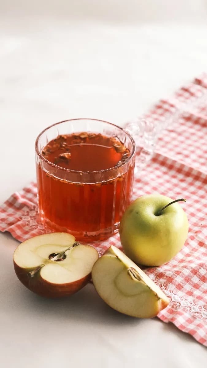 Vaso con agua y vinagre de manzana sobre una mesa de cocina junto a manzanas frescas y una botella de vidrio