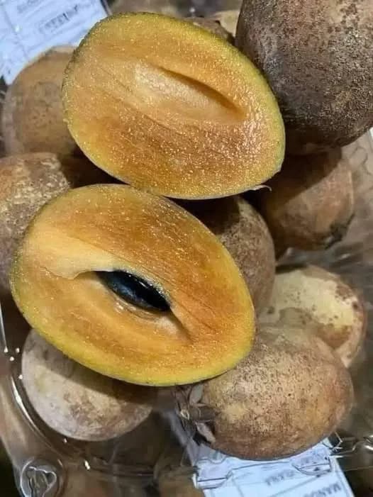 Papaya madura cortada por la mitad con sus semillas negras sobre una mesa de madera, acompañada de rebanadas frescas listas para consumir.