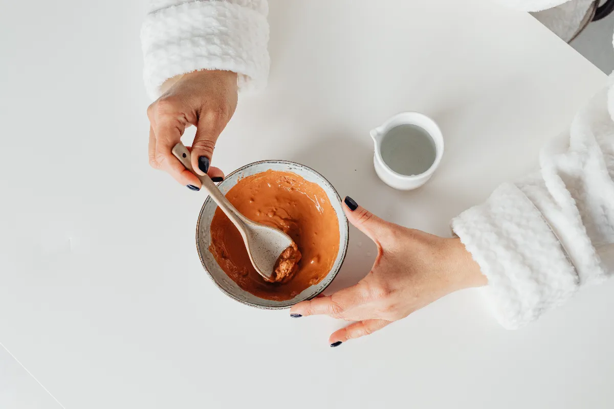 Ingredientes naturales para mascarillas caseras en un tocador: avena, miel, yogur, aloe vera y aguacate junto a un cuenco y una brocha facial.