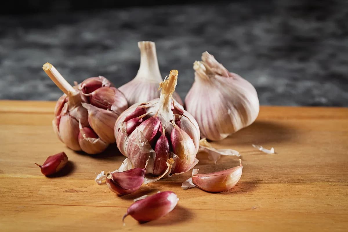 Cabezas de ajo fresco y dientes de ajo pelados sobre una tabla de madera en una cocina casera