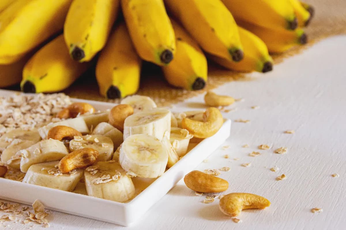 Dos bananas maduras sobre una mesa junto a avena y yogur, representando una merienda saludable y práctica para sumar energía, fibra y potasio.
